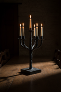 Five-arm hand-forged iron candelabra with twisted arms on dark oak dining table with five lit taper candles, dramatic side lighting