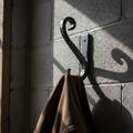 Hand-forged iron coat hook mounted on cinderblock wall with canvas work jacket hanging, dramatic workshop side lighting