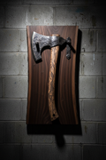 Hand-forged Viking-style axe on black walnut plaque mounted on cinderblock wall, dramatic side lighting on hammer-textured axe head